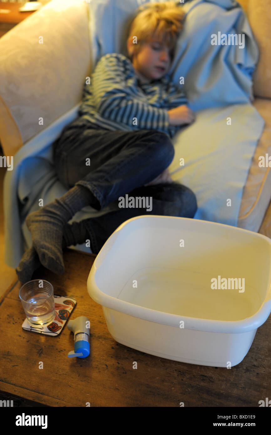 Un bambino malato soffre di inverno vomito bug addormentato su un divano con un vaso malato, vetro di acqua e di inalatore nelle vicinanze Foto Stock
