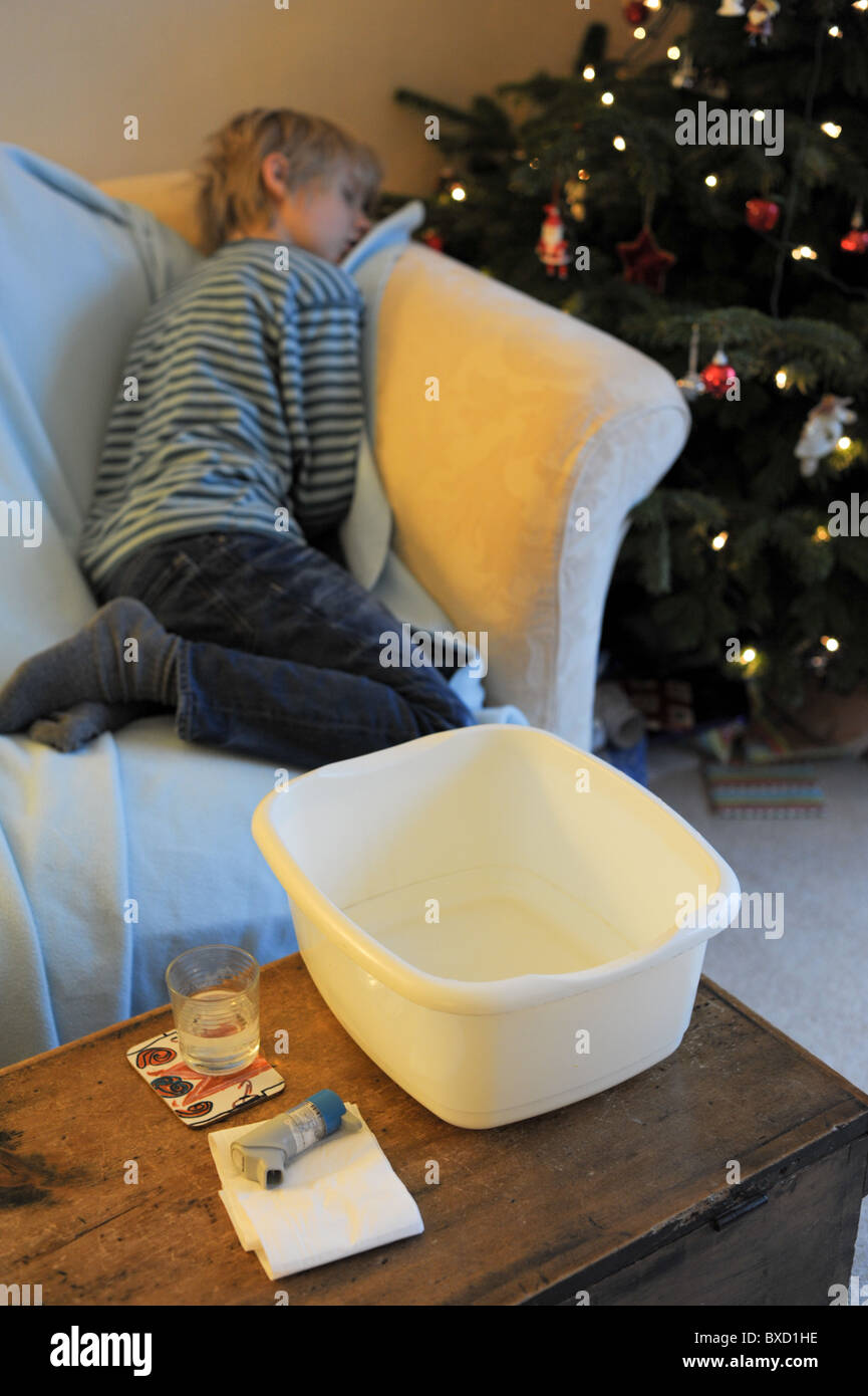 Un bambino malato soffre di inverno vomito bug addormentato su un divano con un albero di Natale con un vaso malato e di tessuti nelle vicinanze Foto Stock