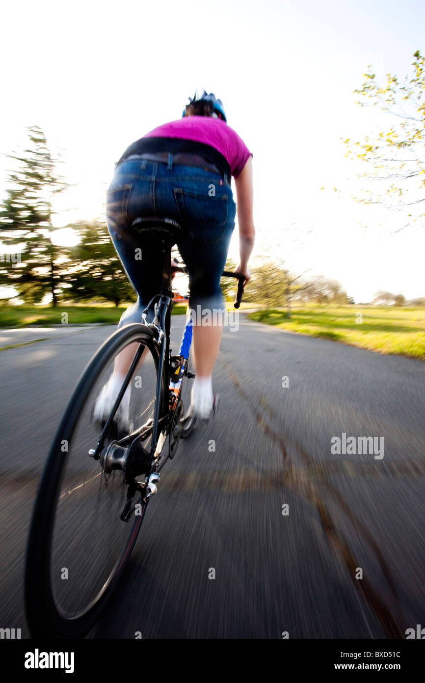 Una giovane donna vanno in bicicletta intorno a un parco al tramonto. Foto Stock