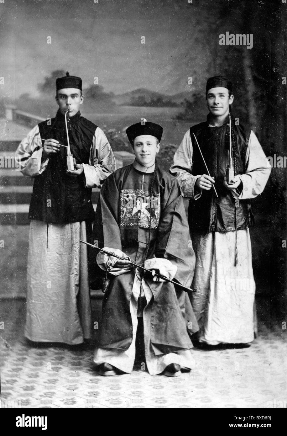 Gli europei o Unione Uomini vestiti in abiti cinesi o di costume, fumatori tubi di oppio, studio foto c1900 di Hong Kong Foto Stock