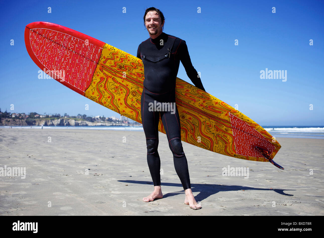 Surfista maschio tenendo un colorato con la tavola da surf in posa per una foto a La Jolla Shores beach. Foto Stock