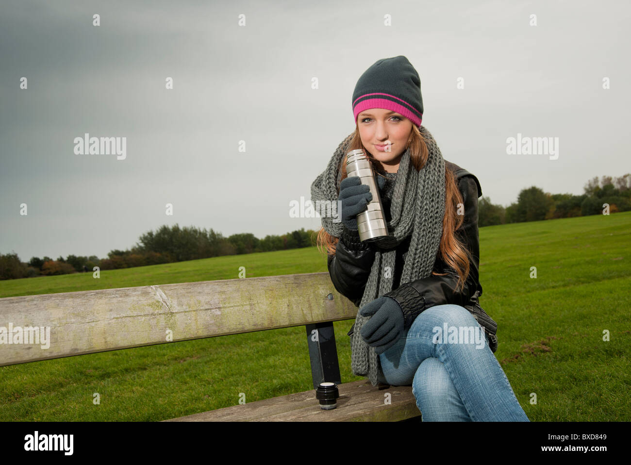 Donna seduta su una panchina avente una bevanda calda da un thermos in autunno Foto Stock
