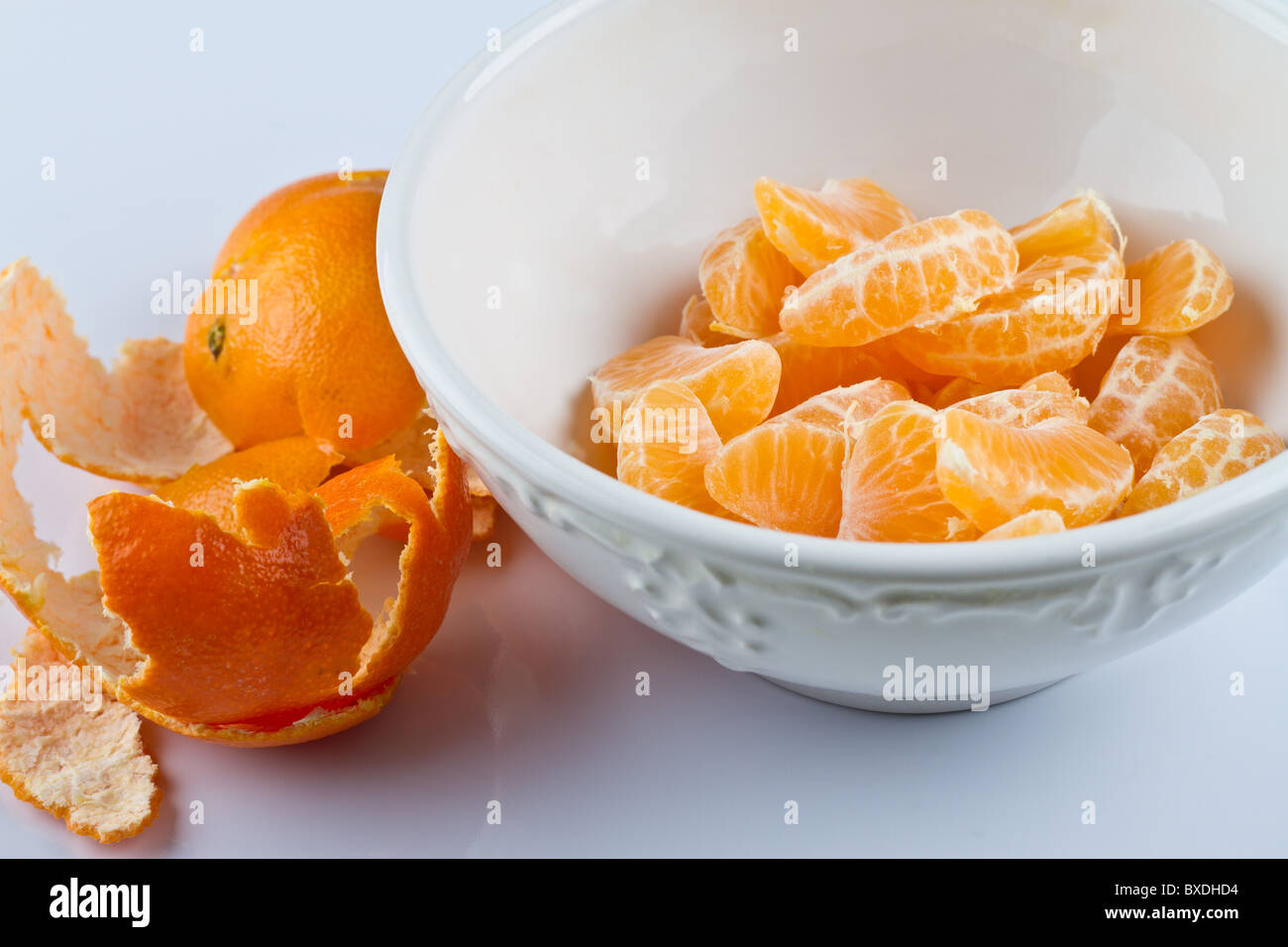 Sbucciate le clementine in vaschetta bianca sulla superficie bianca Foto Stock