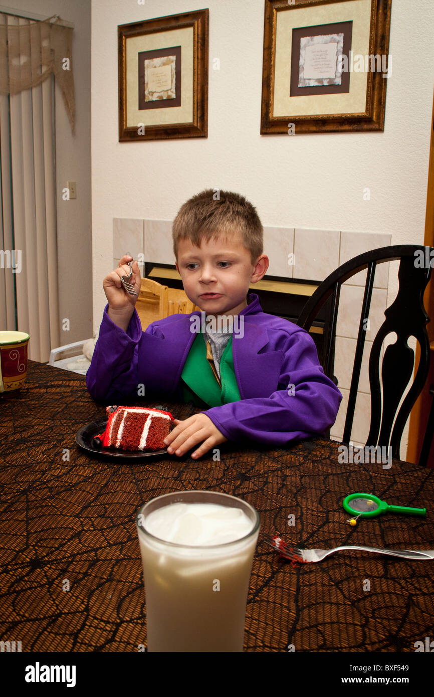 Un giovane ragazzo dolce mangiare e bere latte nel suo costume di Halloween Foto Stock