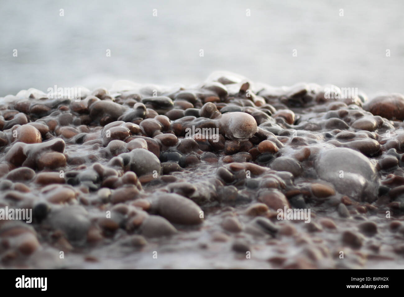 Una chiusura del ghiaccio coperto di ciottoli su una spiaggia sul lago Superiore. Foto Stock