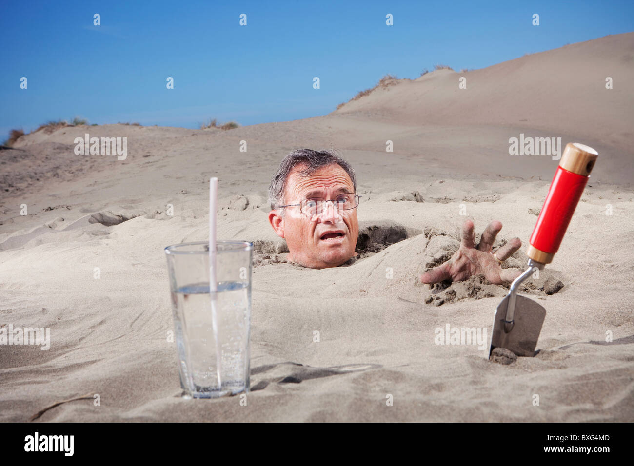 Uomo caucasico sepolto nella sabbia accanto al vetro di acqua e cazzuola Foto Stock
