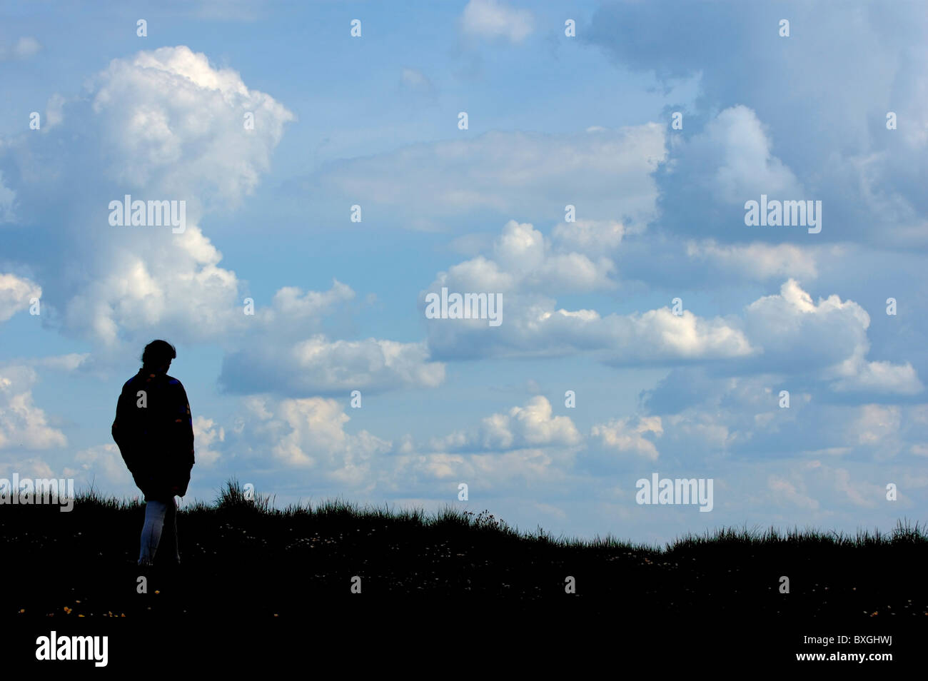 Silhouette di una donna solitarie passeggiate attraverso la campagna sotto un cielo nuvoloso, Francia. Foto Stock