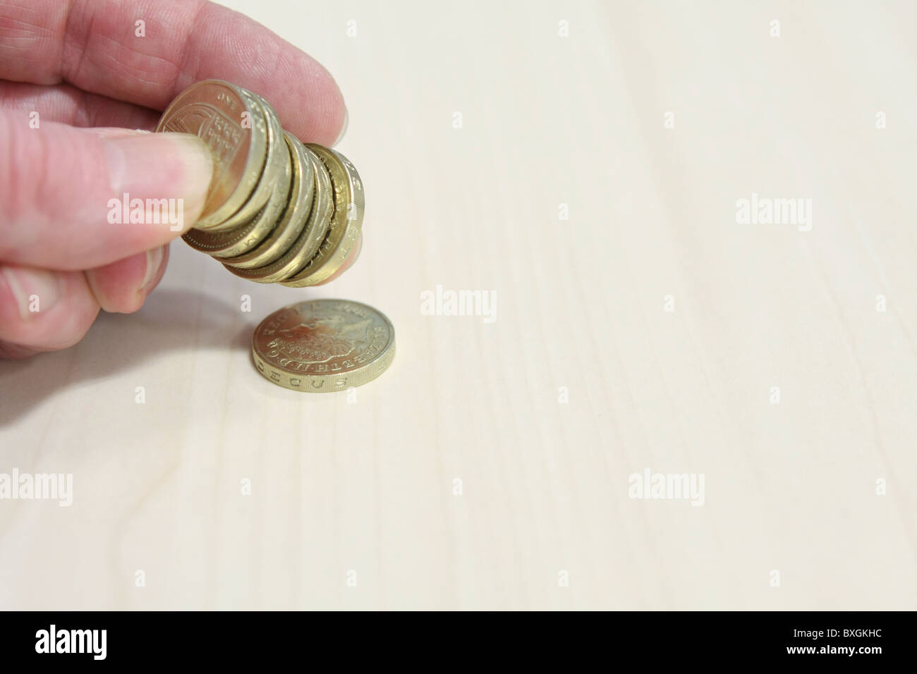 Una pila di sterling £1 monete trattenute tra il dito e il pollice con una moneta allentata Foto Stock