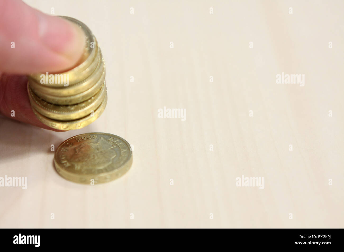Una pila di sterling £1 monete trattenute tra il dito e il pollice con una moneta allentata Foto Stock