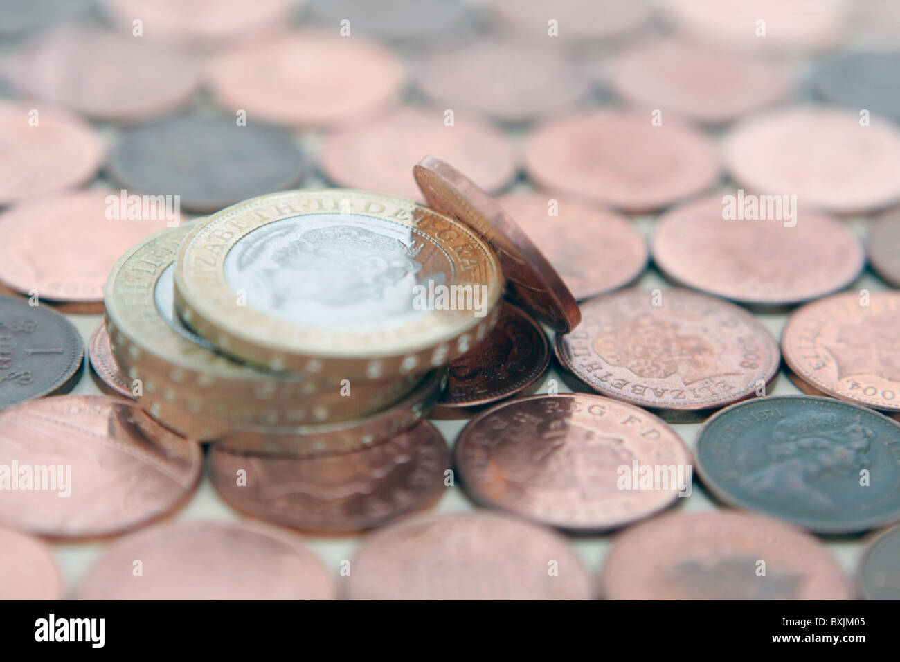 Una sterlina 1p coin appoggiata contro una piccola pila di £ 2 monete - Tutto su uno sfondo di 1p delle monete in euro Foto Stock
