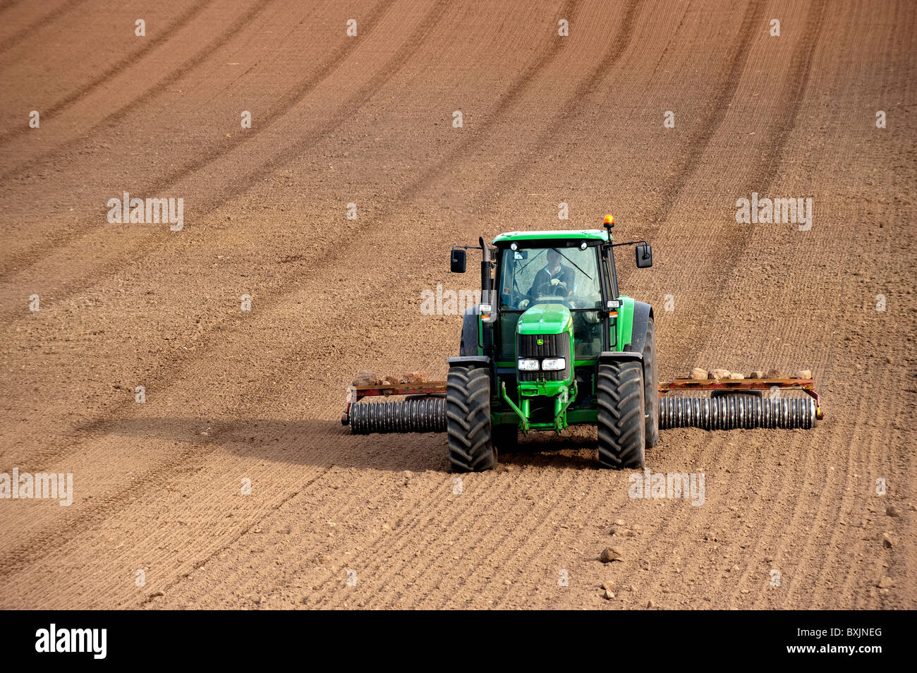 Contadino con terreno premere il rotolamento seedbed, utilizzando trattore John Deere. Kelso, Scozia Foto Stock