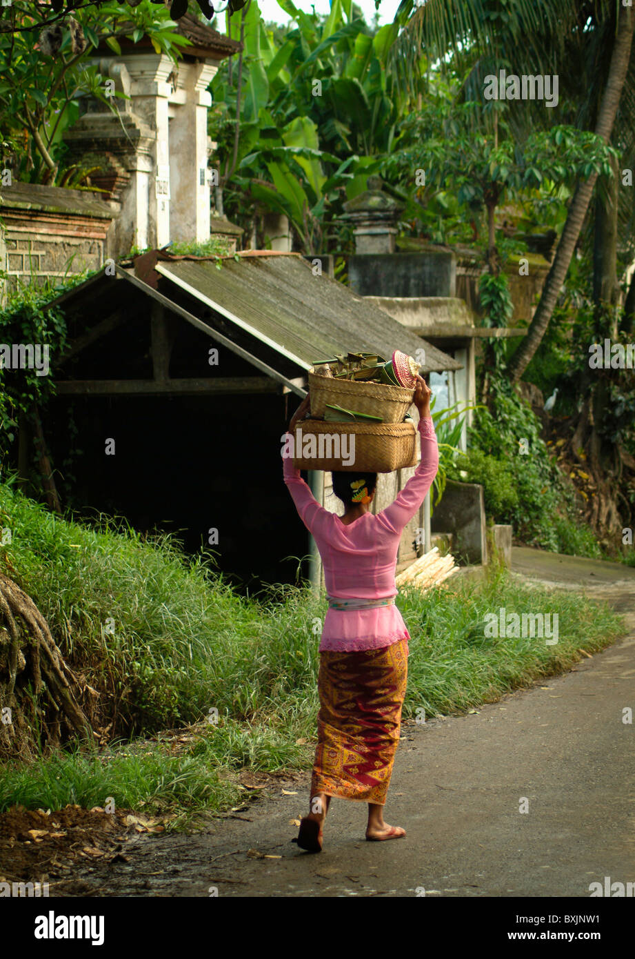 Una donna nel villaggio di Petulu, Bali, torna a casa con dal locale tempio indù con offrendo cestini sul suo capo. Foto Stock