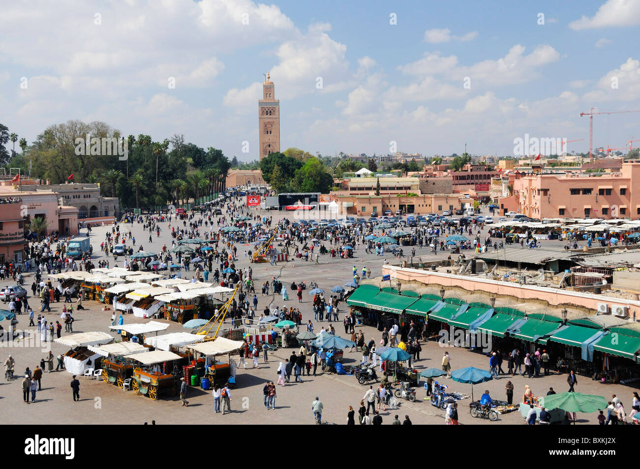 Vista su occupato Djemaa el Fna luogo di incontro con un lontano vista della Moschea Kotoubia in Marrakech Foto Stock