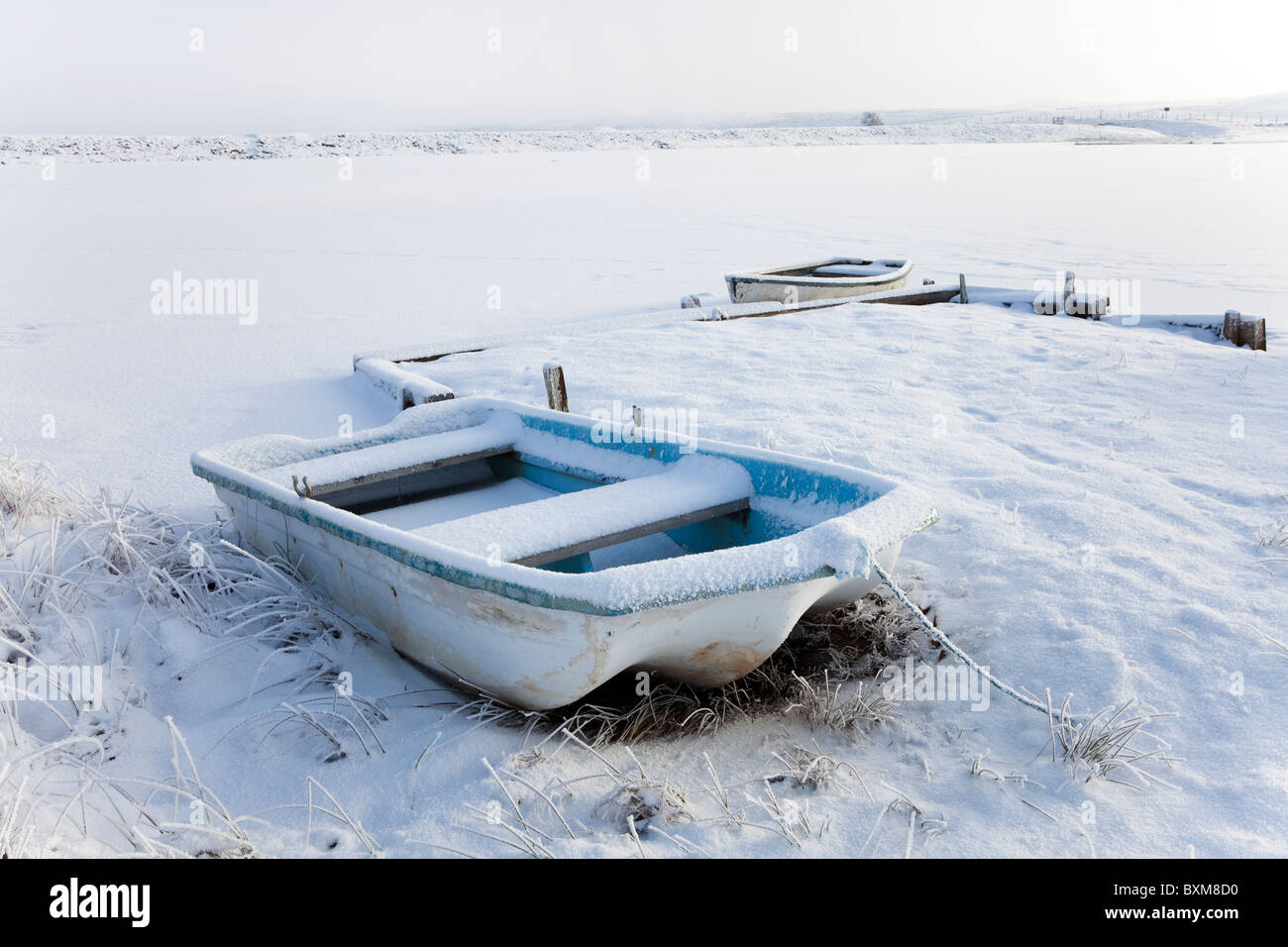 Due imbarcazioni a remi in corrispondenza di un bordo di una loch legato accanto a un piccolo molo. Barche coperte di neve e alcuni frost Foto Stock
