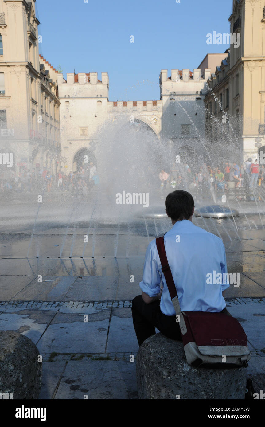 Uomo seduto a Karlsplatz Fountaine a Monaco di Baviera Foto Stock