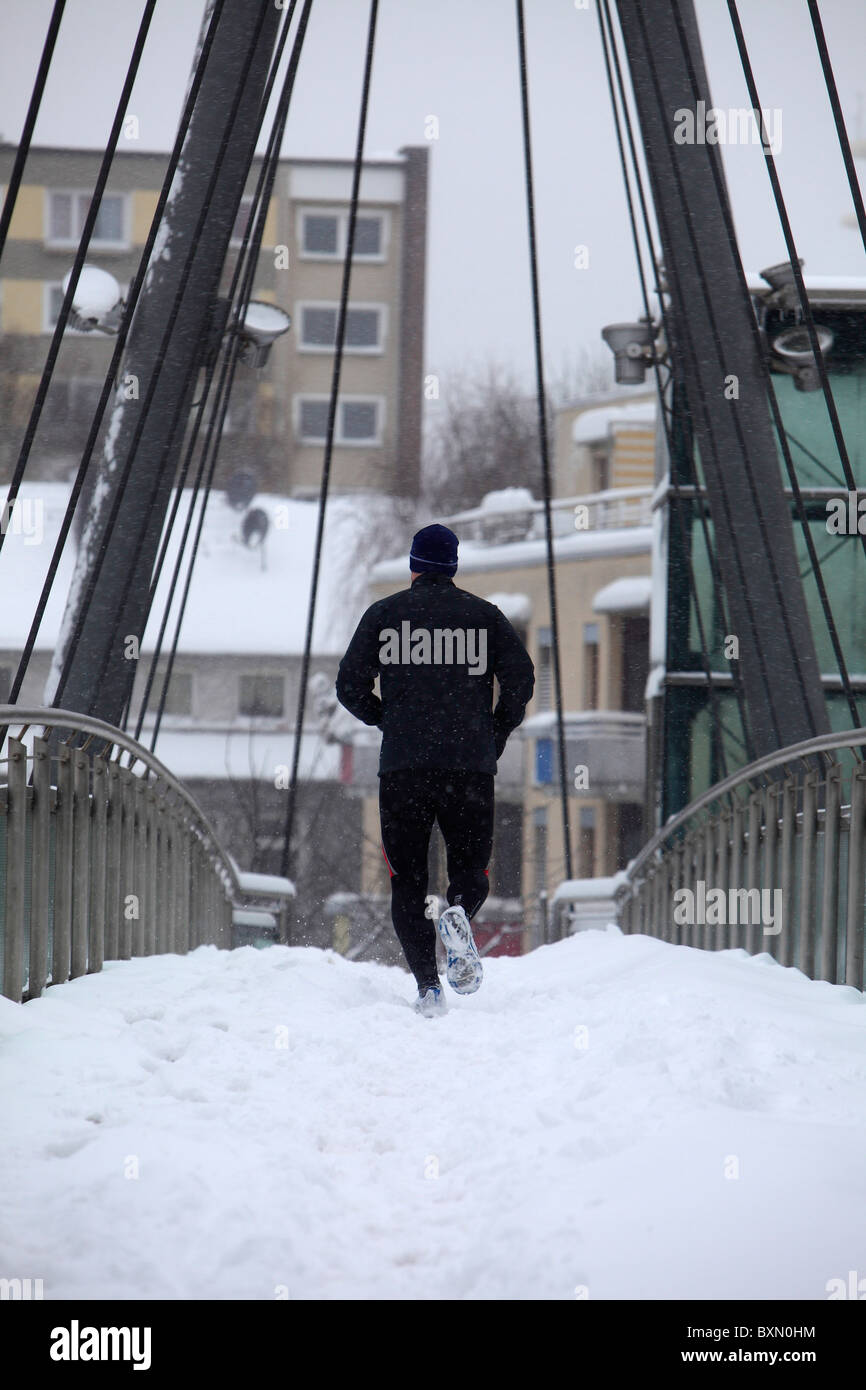L uomo è fare jogging in inverno in una città, su di un ponte pedonale in neve alta. Essen, Germania. Foto Stock
