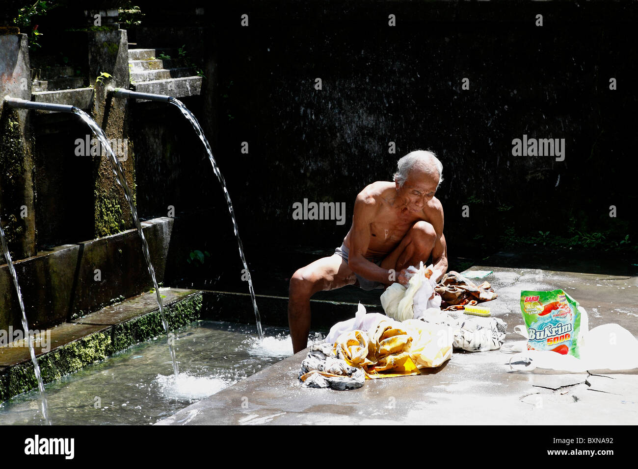 Anziani uomo Balinese lavando i suoi vestiti in una primavera naturale piscina a Pura Gunung Kawi tempio Foto Stock