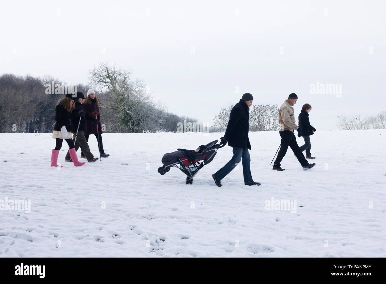 Il trascinamento di un bimbo di buggy come membri della famiglia uscire per una passeggiata in aperta campagna snowbound nel nord Somerset. Foto Stock