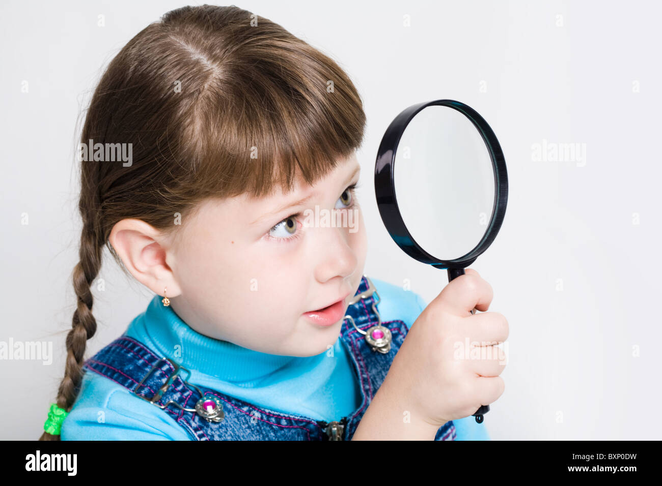 Close-up di piccola ragazza tenendo alla ricerca di vetro in mano e guardare attraverso di esso Foto Stock