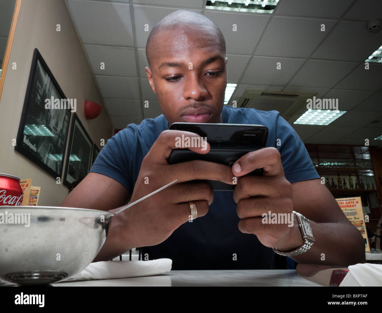L'uomo la lettura di notizie su internet su una smart un cellulare in un ristorante fast food Foto Stock