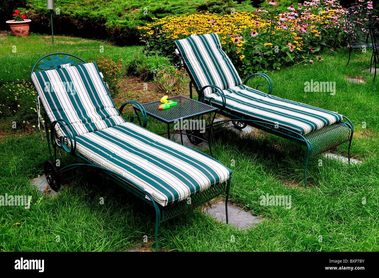 Un caldo giorno d'estate e due sedie strippato in un bellissimo giardino con piscina. Foto Stock