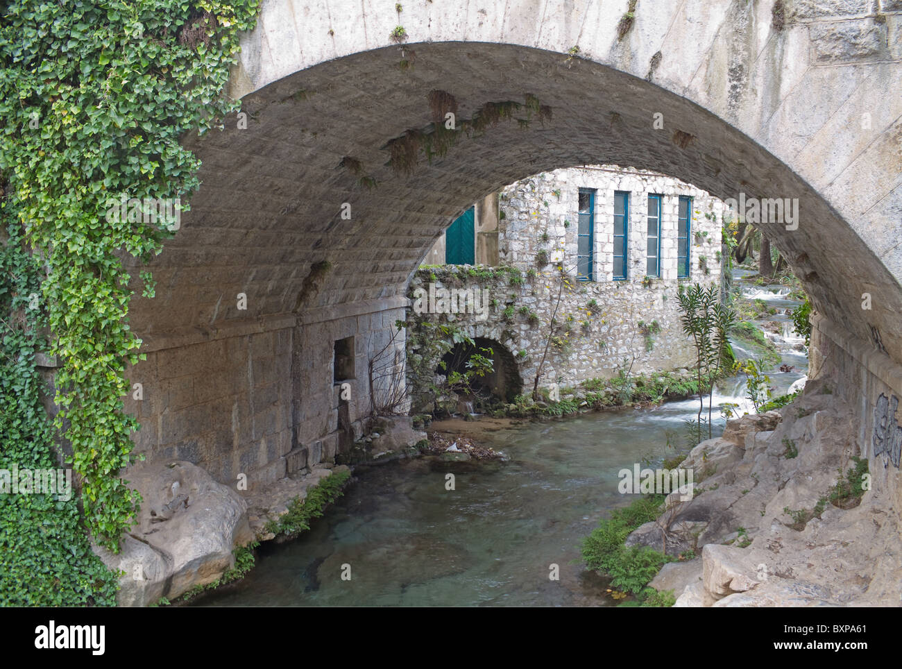 Un piccolo fiume che passa sotto un ponte di pietra nella città di Livadia, Grecia centrale Foto Stock