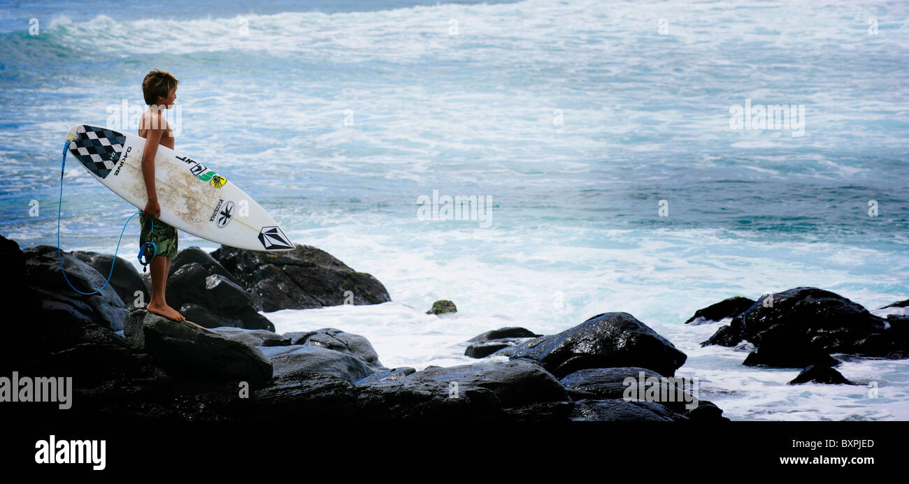 Un giovane surfer guardando il surf break sulle rocce al Parco Hookipa Maui sulle isole Hawaiiano Foto Stock