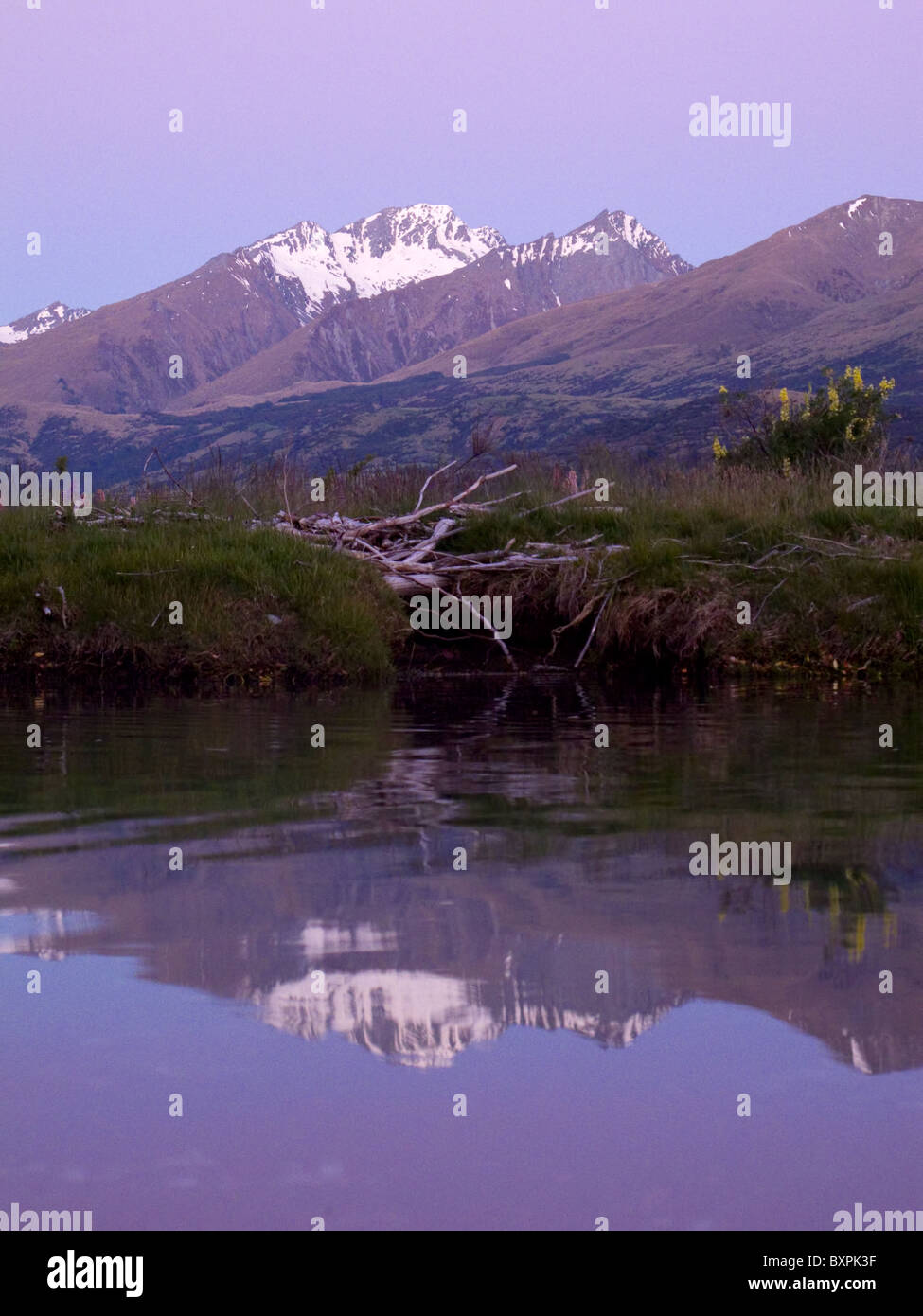 Una montagna ricoperte di neve è relfected nelle acque del Lago Wakatipu nella calda luce della sera Foto Stock