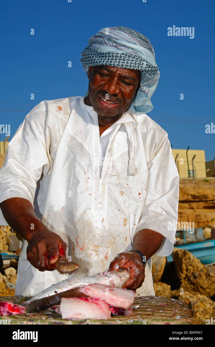 Di carnagione scura pescivendolo il taglio di pesce fresco in un mercato a cielo aperto in stallo, Sur, il sultanato di Oman Foto Stock