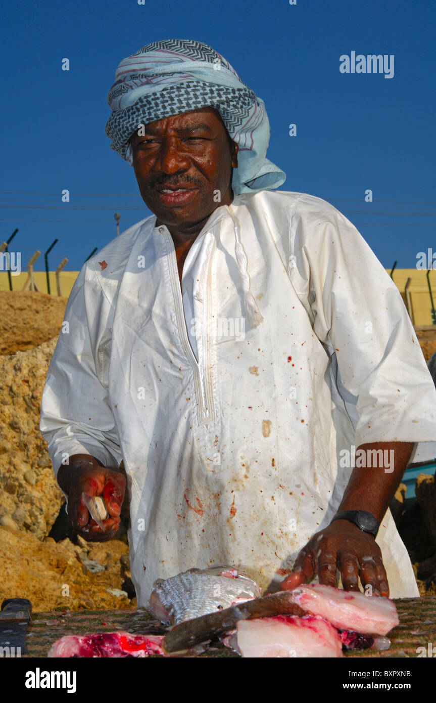 Di carnagione scura pescivendolo il taglio di pesce fresco in un mercato a cielo aperto in stallo, Sur, il sultanato di Oman Foto Stock