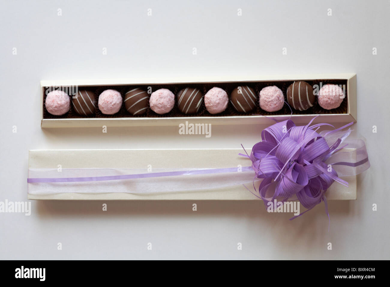 In confezione aperta di fragole e cioccolato cioccolatini al tartufo con coperchio con viola bow rimosso dal lato isolato su sfondo bianco Foto Stock