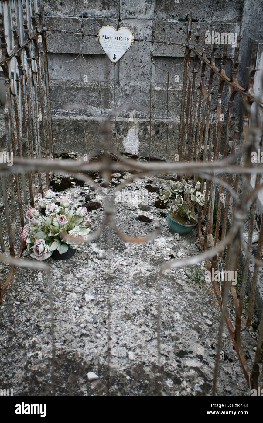 Una vecchia tomba cementato racchiuso da decorativi in metallo con ringhiera a forma di cuore ad ornamento e due weathered fake invasati. Foto Stock