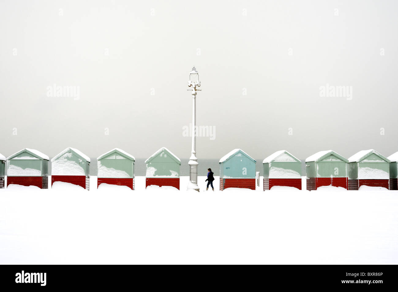 Un viandante passa una fila di capanne spiaggia coperta di neve Foto Stock