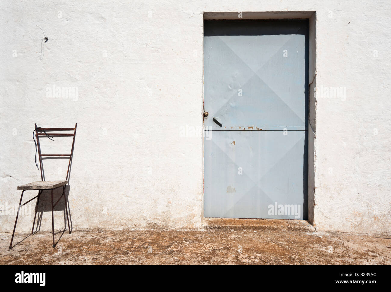 Ferro battuto sedia contro una parete bianca, Ostuni, Puglia, Italia Foto Stock