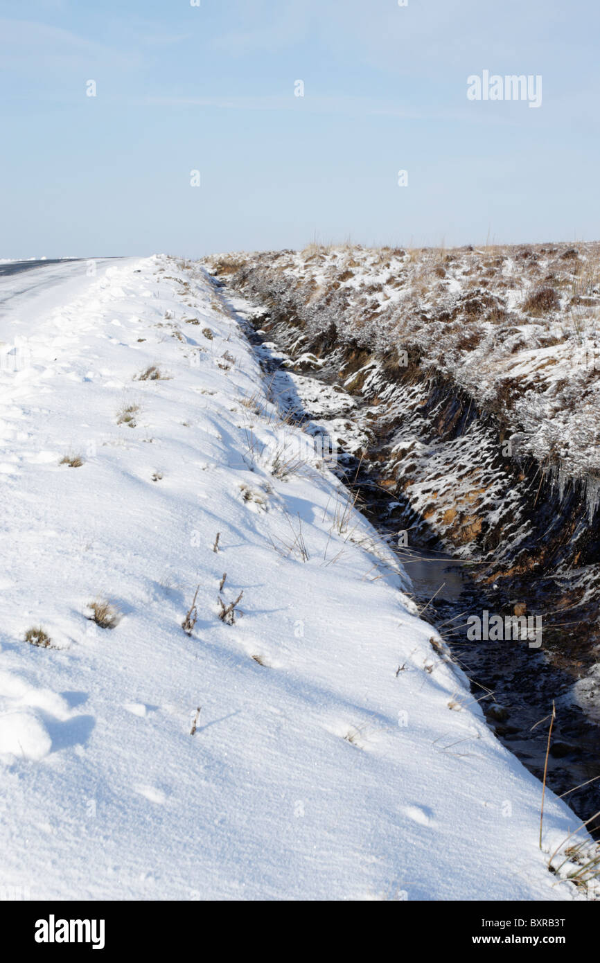 Il fosso di drenaggio in corrispondenza del bordo di erica moor che costeggia una strada con i ghiaccioli che mostrano evidenza di drenaggio dell'acqua in esso Foto Stock