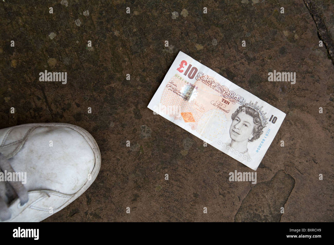 10 dieci sterlina inglese money bank nota sul marciapiede accanto a un bianco scarpa trainer Foto Stock