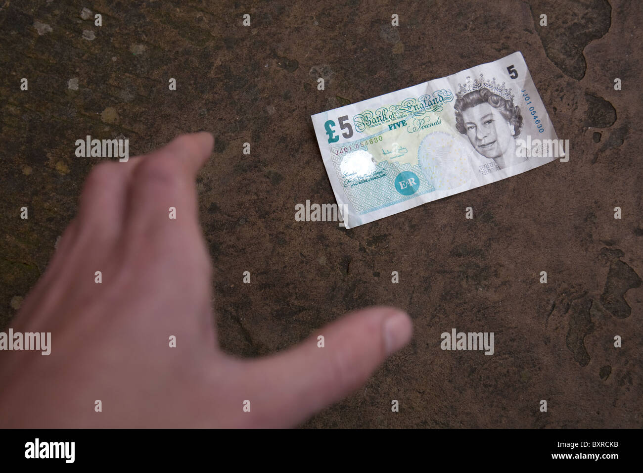 La mano di raggiungere per prelevare una caduta di cinque 5 Pound sterling bank nota a terra su un marciapiede Foto Stock