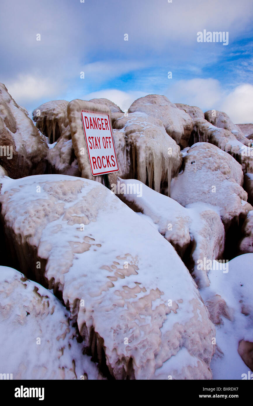 Segnale di avvertimento sulle rocce ghiacciate lungo una struttura di frangionde vicino alla riva del lago Erie, OHIO USA Foto Stock