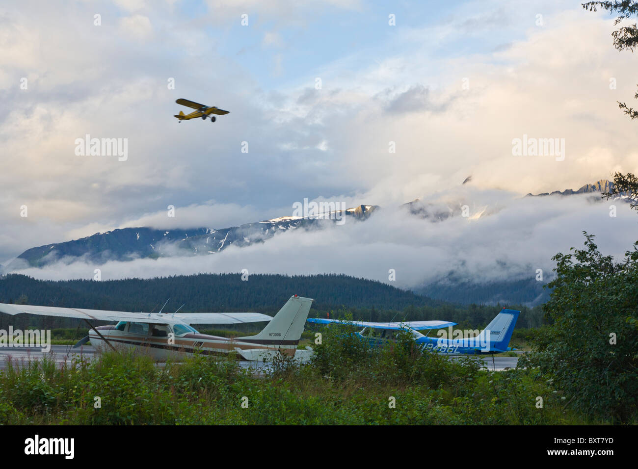 Piccoli aerei parcheggiati sul terreno con piccolo aereo nel cielo aganist nuvole basse in mounatins in Seward Alaska Foto Stock