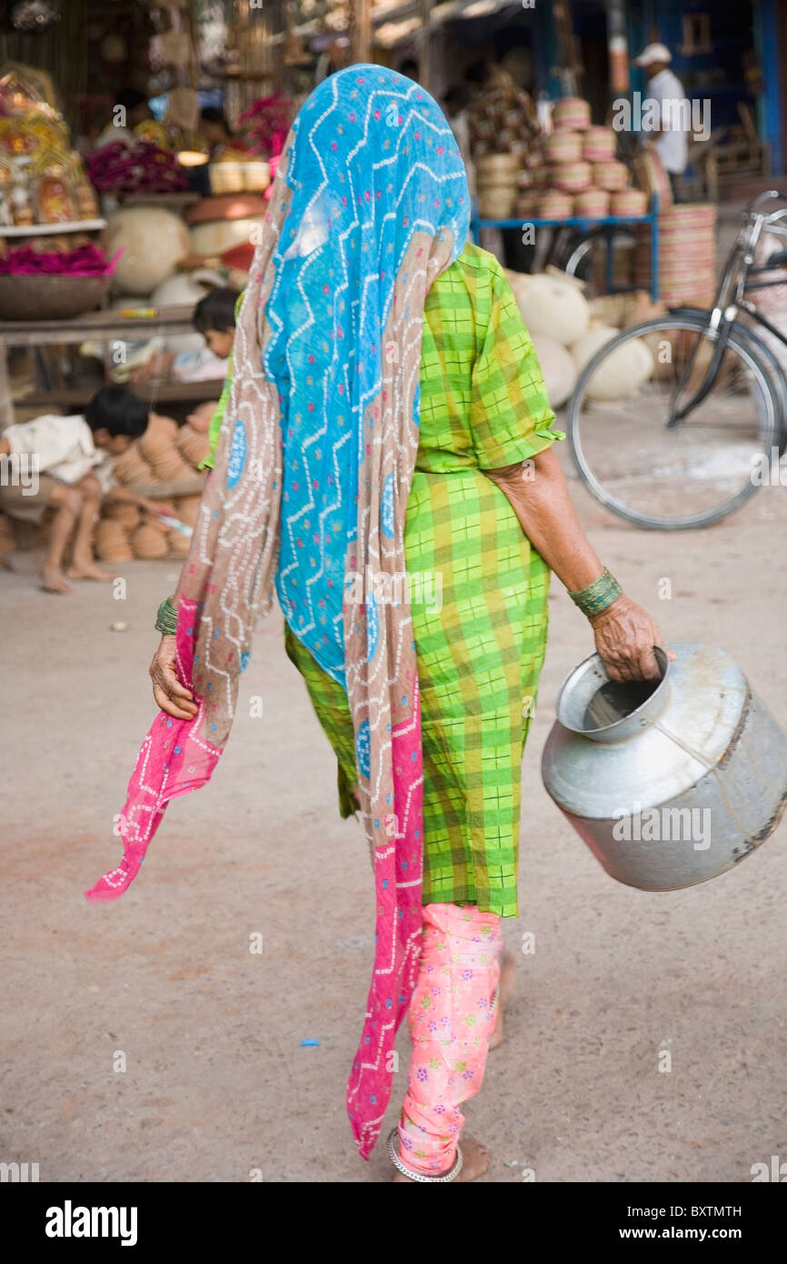 Donna in sari colorati che porta una brocca in metallo Foto Stock