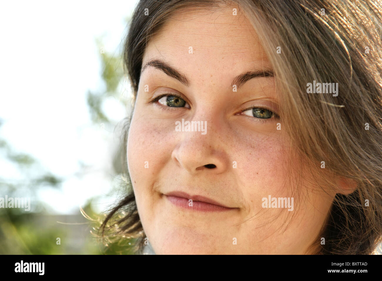 Real giovane donna ritratto preso al di fuori, ha un po' sarcastico sorriso con le sopracciglia sollevate. Gli occhi sono multicolori. Foto Stock