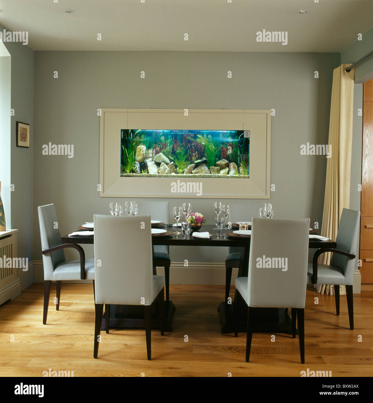 Acquario impostato nella parete della sala da pranzo moderna con alti-retro bianco sedie imbottite in tavola nera Foto Stock
