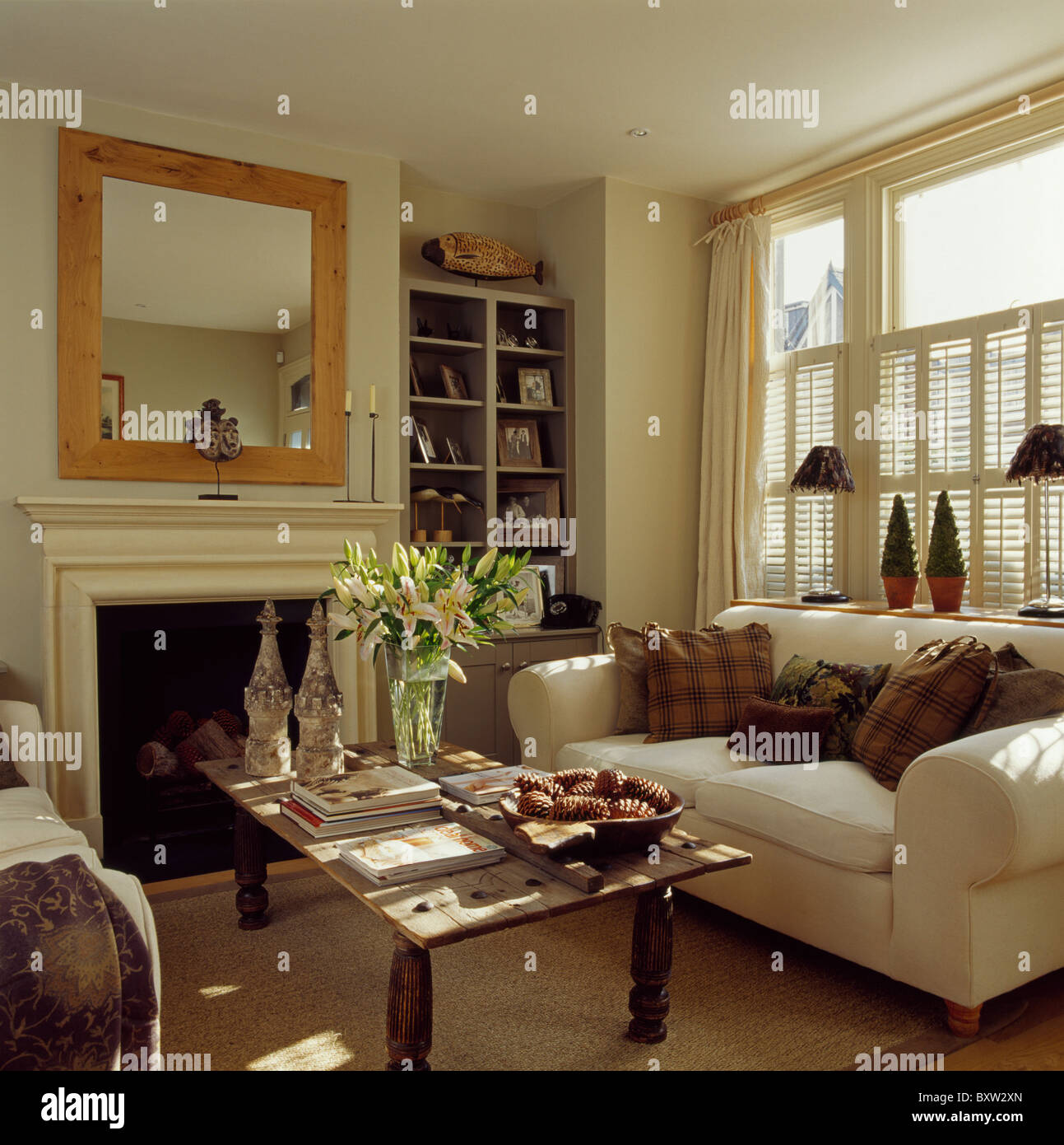 Cuscini marrone sul divano color crema sotto la finestra con la crema  persiane in stile piantagione in soggiorno con legno-specchio incorniciato  sopra il camino Foto stock - Alamy