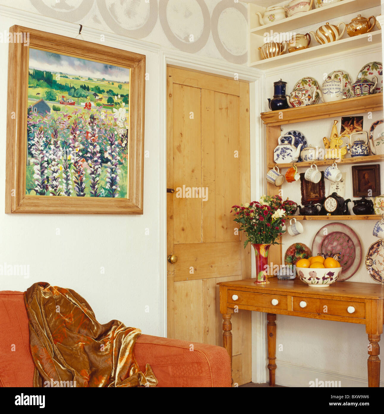 Grande immagine accanto a pini porta in piccolo soggiorno con una collezione di teiere su ripiani sopra antico tavolo console Foto Stock