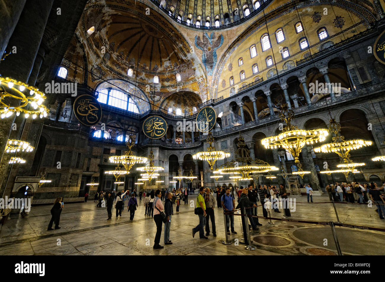 Duomo interno di Santa Sofia e lampadari Istanbul Turchia // ISTANBUL, Turchia - la vasta sala principale di Santa Sofia mostra il suo notevole design architettonico bizantino, con la sua imponente cupola centrale supportata da pendenti e semi-cupole. L'interno presenta elementi cristiani e islamici, tra cui mosaici bizantini, calligrafia ottomana e grandi avize ottomane (lampadari). Enormi colonne e pannelli in marmo rivestono lo spazio, dimostrando la grandezza dell'ingegneria architettonica del vi secolo. Foto Stock