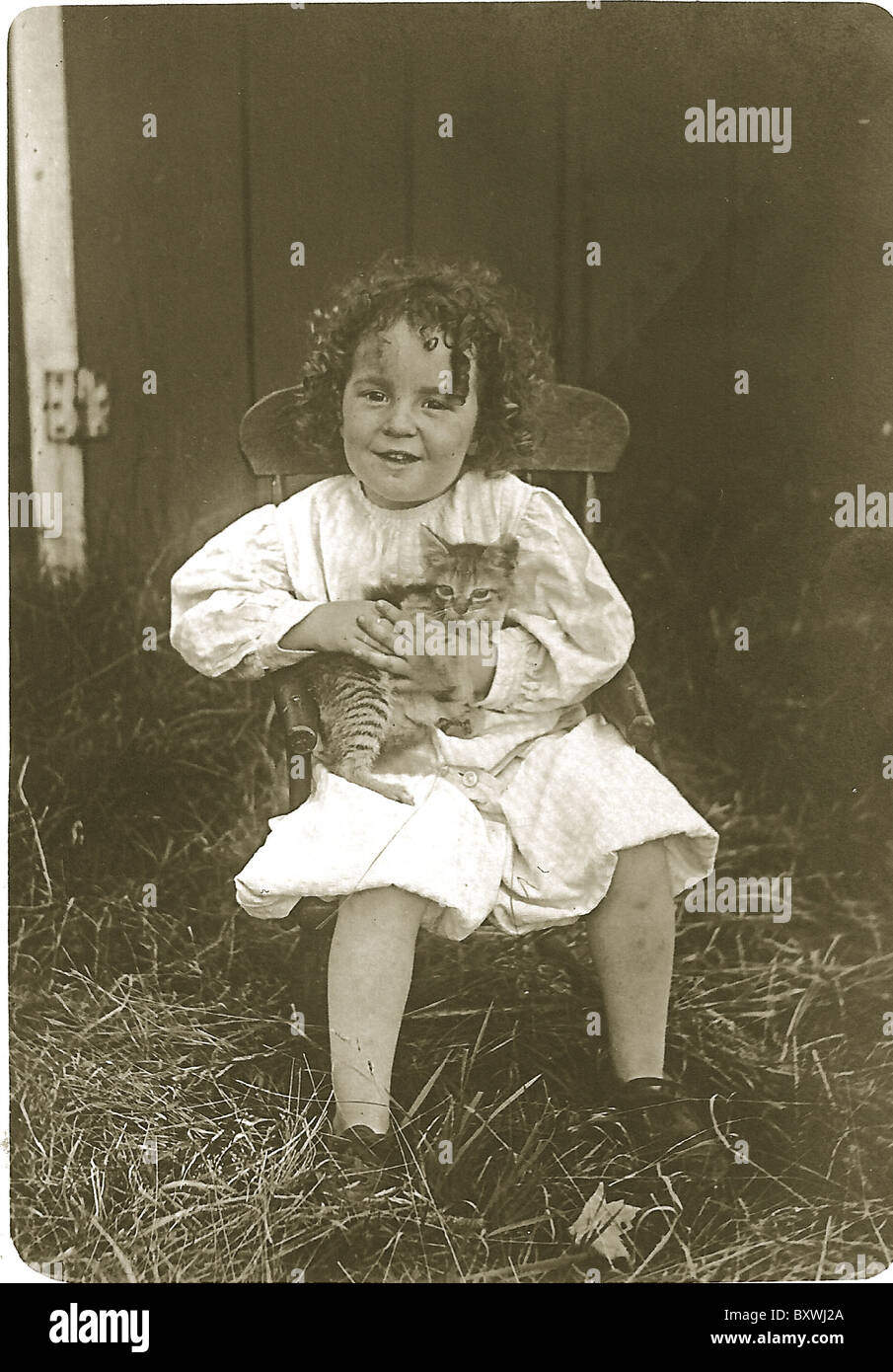 Foto antica di bambino con capelli ricci che tiene gattino nel fienile c. 1910-1920 Foto Stock