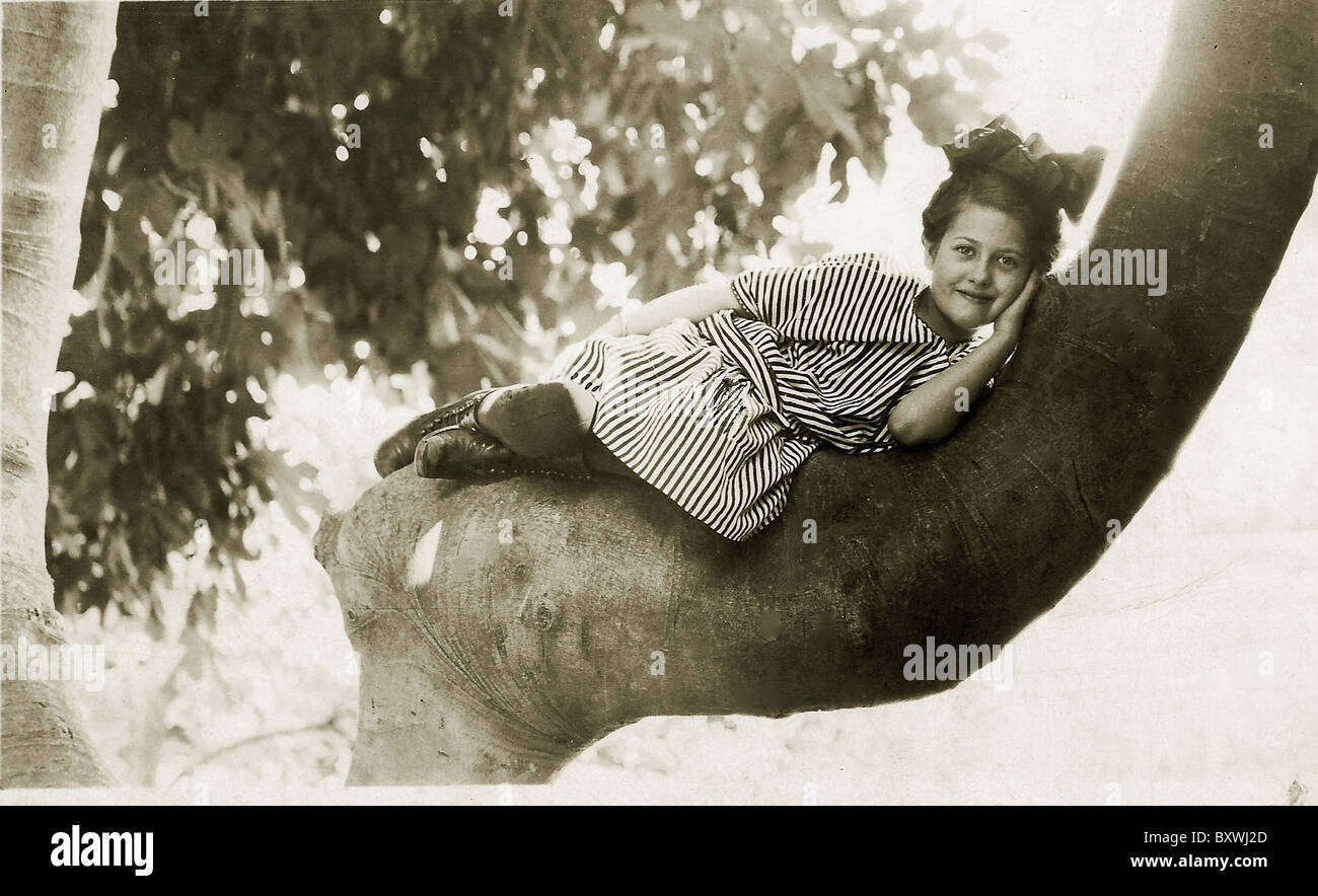 Foto di antiquariato di "piccola ragazza con grande arco rilassante in una struttura ad albero. c. 1910-1915. Foto Stock
