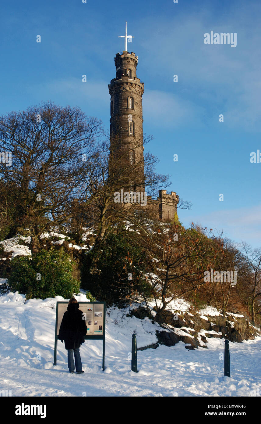 Una solitaria figura legge la scheda di informazioni accanto a Nelson's monumento su Calton Hill a Edimburgo, Scozia, Regno Unito Foto Stock