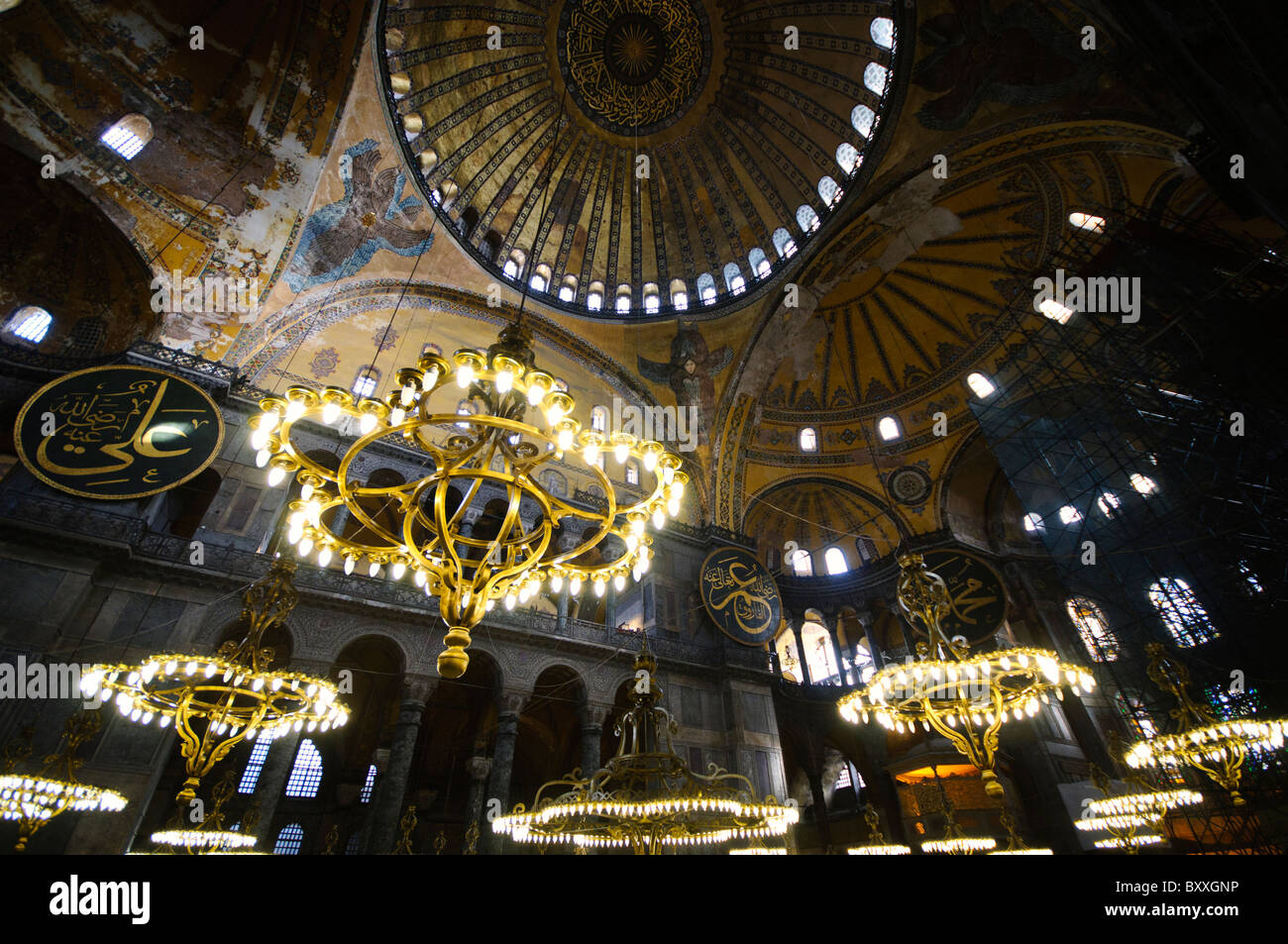 Lampadari della cupola interna di Hagia Sophia Istanbul Turchia // ISTANBUL, Turchia - la vasta sala principale di Hagia Sophia mostra il suo notevole design architettonico bizantino, con la sua imponente cupola centrale supportata da pendenti e semi-cupole. L'interno presenta elementi cristiani e islamici, tra cui mosaici bizantini, calligrafia ottomana e grandi avize ottomane (lampadari). Enormi colonne e pannelli in marmo rivestono lo spazio, dimostrando la grandezza dell'ingegneria architettonica del vi secolo. Foto Stock