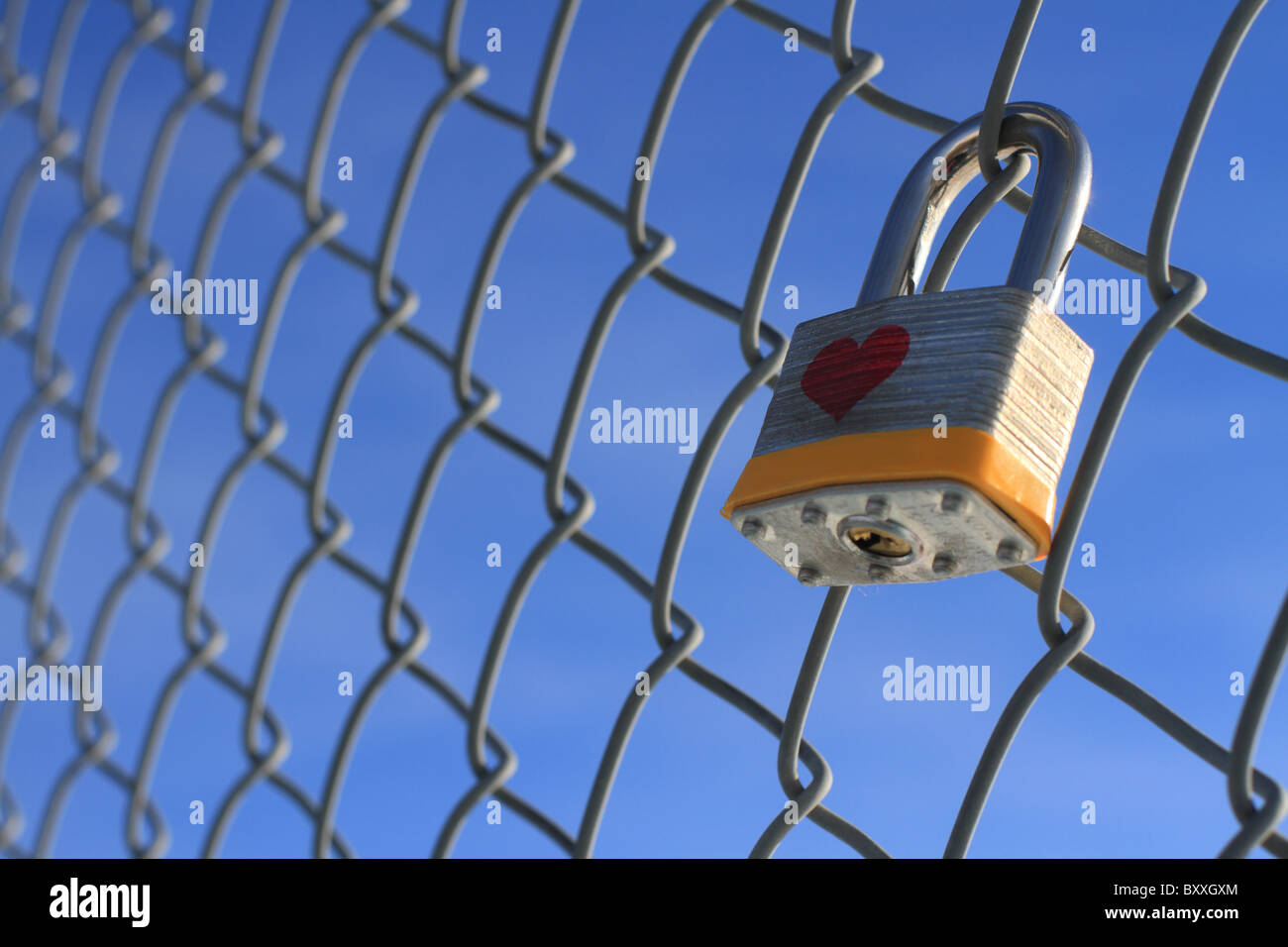 Lucchetto Chiuso con cuore appeso a una catena di recinzione collegati con un cielo blu in background. Foto Stock